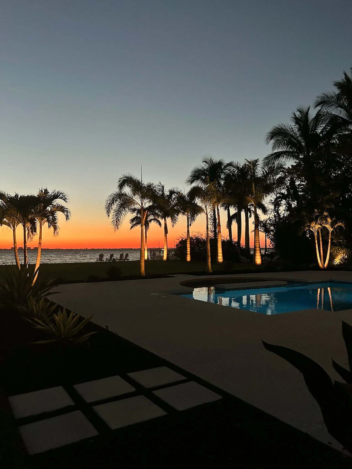 Uplit palms along a waterfront lawn with the bay glowing at sunset