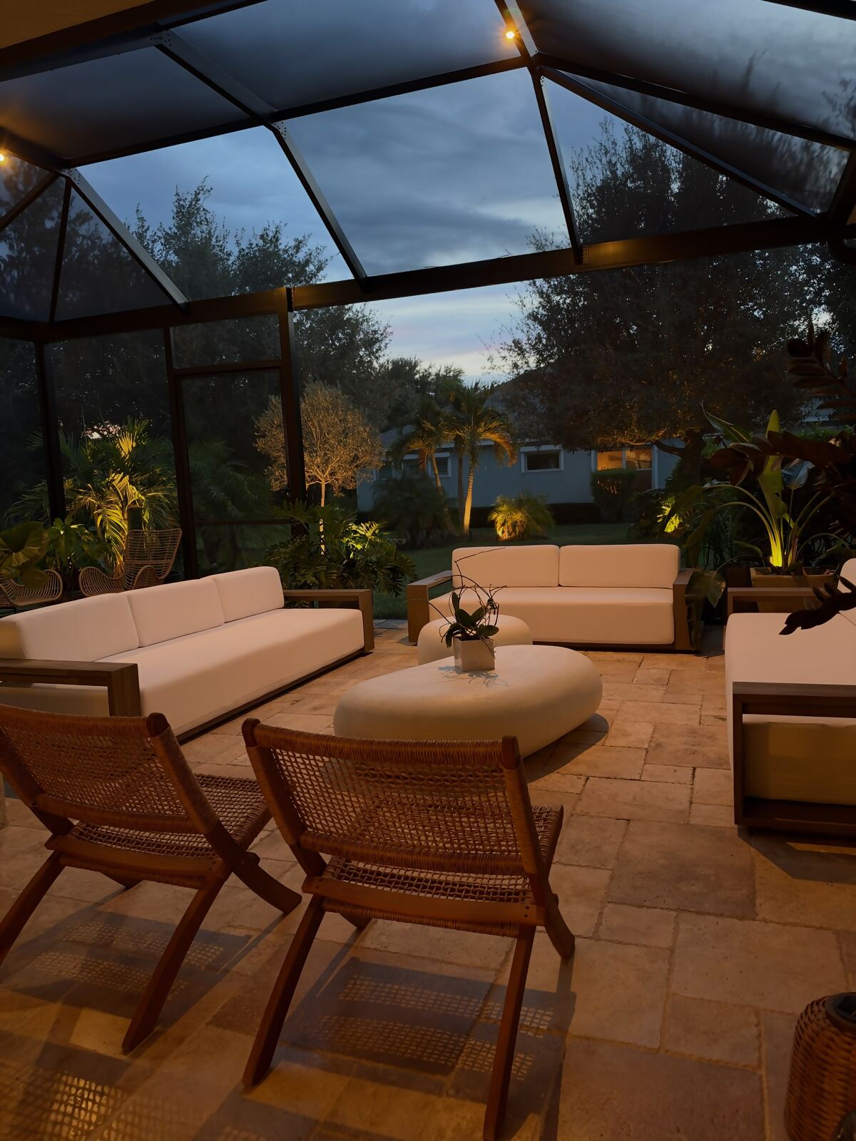 Screened pool cage lanai with warm overhead lighting over outdoor sofas at dusk